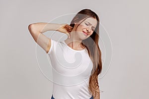 Unhealthy woman standing massaging neck to relieve pain, muscle strain in back.