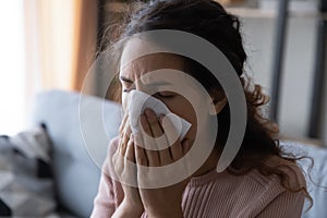 Unhealthy young lady using paper tissue, wiping runny nose. photo
