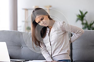 Unhealthy young woman sitting on couch suffers from back pain