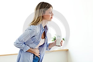 Unhealthy young woman with stomachache holding a glass with milk at home.