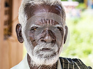 An unidentifed old senior indian poor man portrait with a dark brown wrinkled face and white hair and a white beard, looks serious