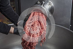 Unidentifiable butcher holding tray full of minced raw red meat leaving machine in food processing plant