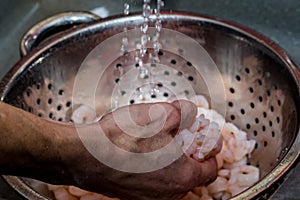 Unidentifiable chef defrosting prawns under cold running water
