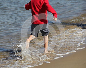 An unidentifiable child runs along the seashore in bare feet, sp