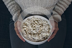 Unidentifiable female holding bowl of popcorn on her lap.