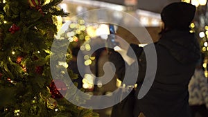 Unidentifiable girl photographs a Christmas tree . View through New Year`s tree