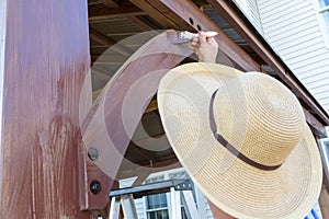 Unidentifiable man in a sunhat staining wood