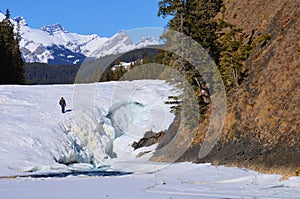 An unidentifiable man walking on a frozen bow fall in Banff National Park in canadian Rocky Mountain,