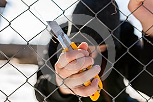 Unidentifiable teenage boy behind wired fence holding a paperknife at correctional institute