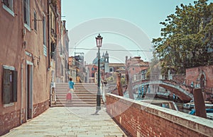 unidentifiable tourist woman with a luggage trolley crossing a bridge over a water canal in Venice, Italy