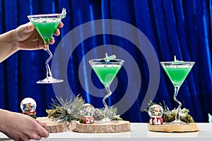 Unidentified barman holding martini glass with Christmas cocktail on blue background