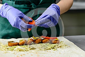 Unidentified chef preparing Falafel roll with sauce, pickles and