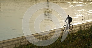 An unidentified cyclist cycles along the riverbank.