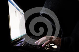 Unidentified Hacker in Black Hood using Laptop Computer in the Dark