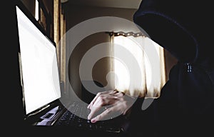 Unidentified Hacker in Black Hood using Laptop Computer in dark room. Selective focus