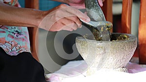 Unidentified human hand pounding spices in stone mortar, traditional Thai curry