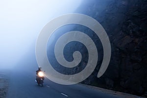 An unidentified male riding motorcycle on the dark misty mountain road, mystic asphalt road in mountain gorge