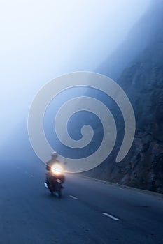 An unidentified male riding motorcycle on the dark misty mountain road, mystic asphalt road in mountain gorge
