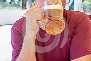 An unidentified man drinks out of a large glass mug of light beer on the background of a pub on a wooden table