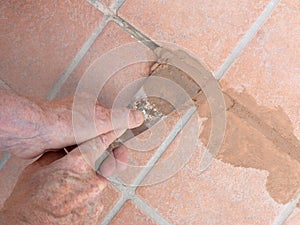 Unidentified man, workman, repairing grout between outdoor terracotta style patio tiles. Closeup detail.