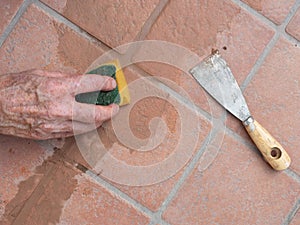 Unidentified man, workman, sponging down repaired grout between outdoor terracotta style patio tiles. Closeup detail.