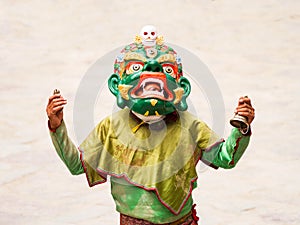 Unidentified monk with ritual bell and vajra performs a religious masked and costumed mystery dance of Tibetan Buddhism during the