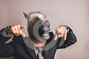 Unidentified person with a dark grey suit and tie wearing a horse mask pointing at the camera