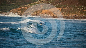 Unidentified surfers riding the rolling waves at Sennen Cove in Cornwall during late sunset