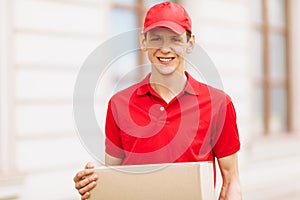 A uniformed courier holds an empty cardboard box in the open air. Delivery service