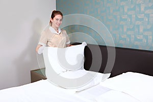 A uniformed maid changes bed linen in an expensive hotel room. Hands in white cotton gloves. The girl smiles and holds a pillow in