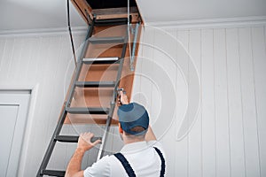 A uniformed specialist fixes a metal ladder to the hatch of the attic door