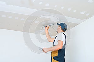 A uniformed worker applies putty to the drywall ceiling. Putty of joints of drywall sheets photo