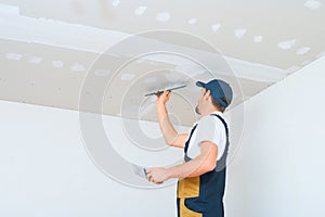 A uniformed worker applies putty to the drywall ceiling. Putty of joints of drywall sheets