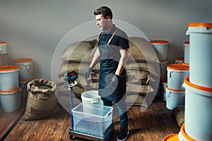 Uniformed worker weighs roasted coffee in a transparent tray on a scale in a coffee industry warehouse with bags and white buckets photo