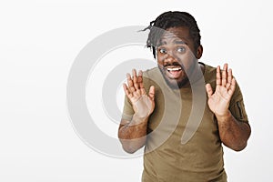 Uninvolved attractive african american guy with braid haircut raising palms in surrender and gazing timid at camera