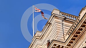 Union Jack Flag flying high above traditional London buildings with a deep blue sky in the background