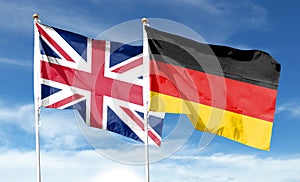 Union Jack and German flag on cloudy sky.