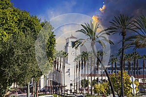 Union Station train station surrounded by office buildings, parked cars, tall lush green palm trees and plants and people walking