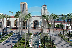Union Station train station surrounded by office buildings, parked cars, tall lush green palm trees and plants and people walking