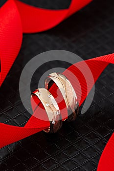 Unique design wedding rings on black background with red ribbon