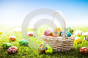 Unique hand painted Easter eggs in basket and lying on grass, blue sky