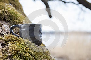 Unique handmade cup with folk sign on moss with blurred lake on background