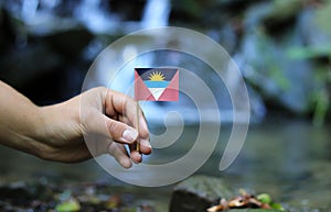 Unique national flag of Antigua and Barbuda with sea and sunrise on wooden stick nad water background. Some hand holds flag and