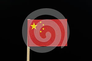 A unique and simply flag of China on toothpick on black background. A large golden star within an arc of four smaller golden stars