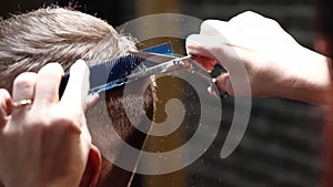 Unisex hairdresser cuts man hair using scissors and comb
