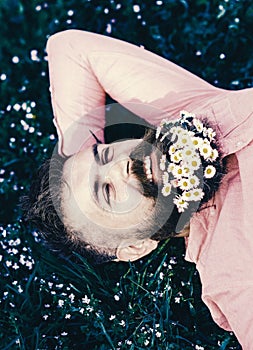 Unite with nature concept. Bearded man with daisy flowers lay on grassplot, grass background. Man with beard on smiling