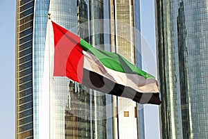 united arab emirates (uae) national flag waves on air in the sky in front of tall buildings in abu dhabi