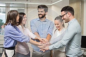 United coworkers standing with their hands together in modern office.