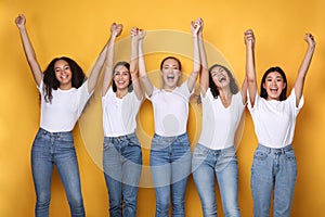 United Diverse Girls Holding Raised Hands Smiling Over Yellow Background