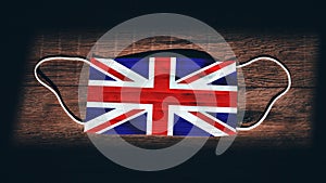 United Kingdom National Flag at medical, surgical, protection mask on black wooden background. Coronavirus Covidâ€“19, Prevent